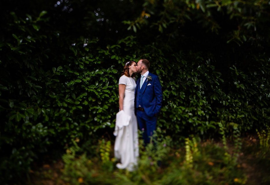 Bride and groom embracing at outdoor wedding with photographer in background