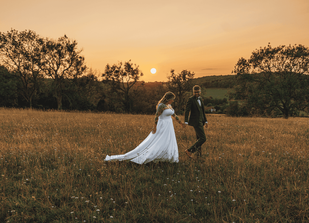 Newly weds walking in field at sunset