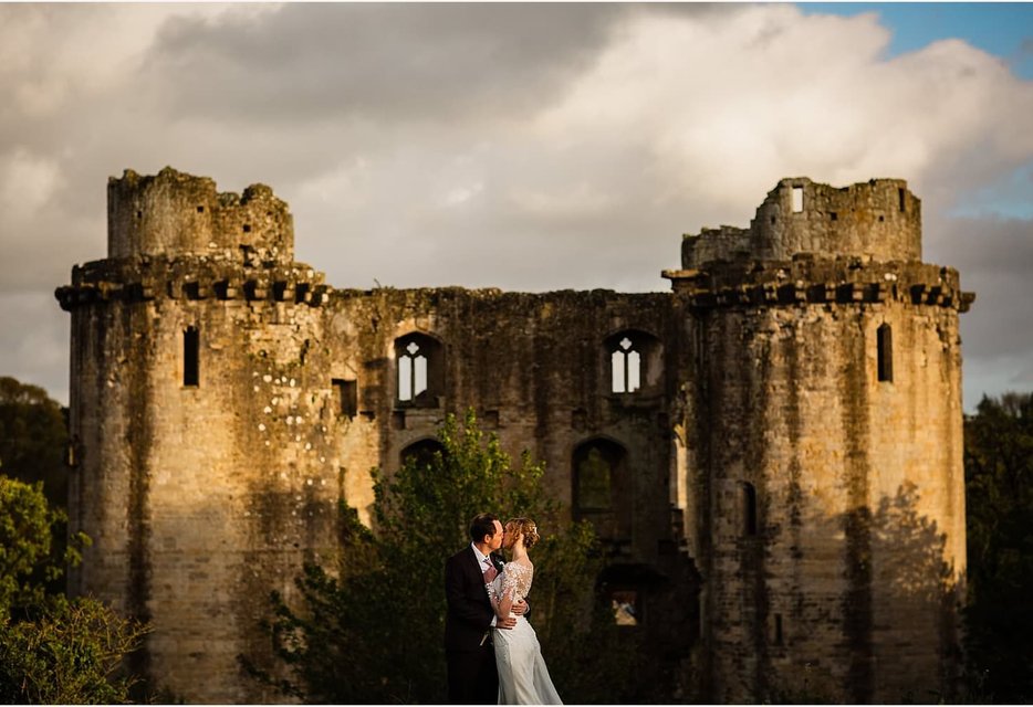 Bride and groom at Nunney Castle ruins with dramatic sky