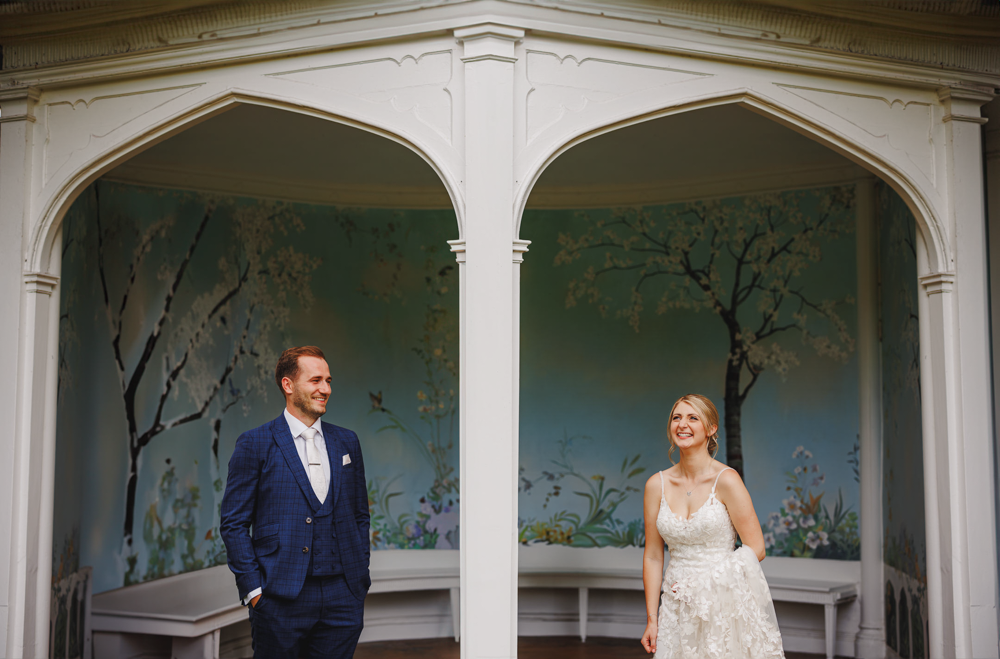Bride and groom under ornate archway with painted mural at Wasing Park