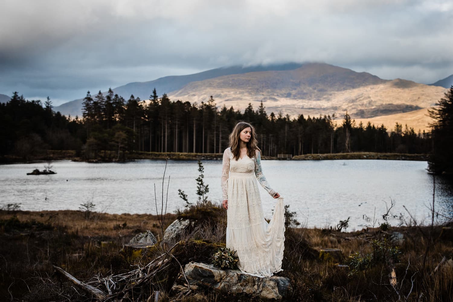 Bride silhouetted against mountain lake at sunset