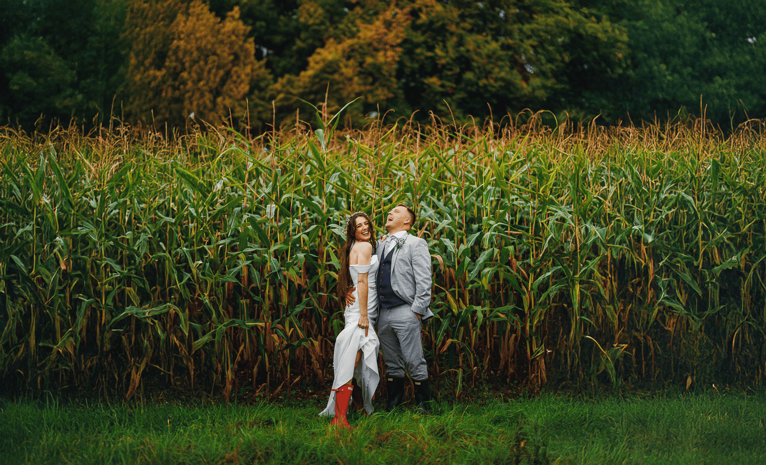 Bride and groom laughing in cornfields, bride showing off her wellies