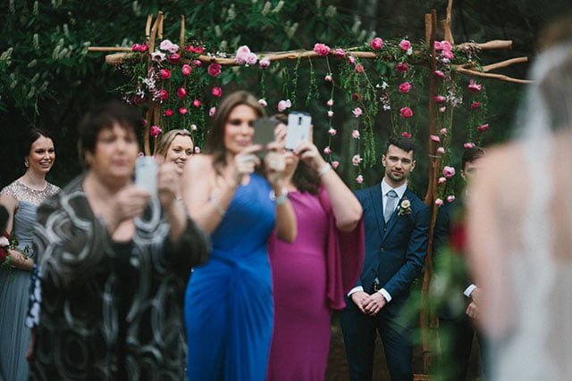 Guest holding phone up during ceremony blocking view of other guests